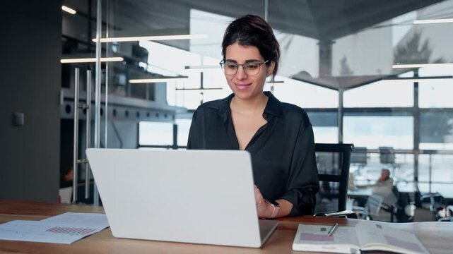 Young middle eastern or indian businesswoman in formal clothes and eyeglasses sitting at desk workplace working on computer. Latin business entrepreneur woman it specialist typing, browsing in office - Powered by Adobe