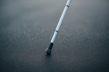 White cane resting on textured asphalt in sunlight: accessibility and independence concept