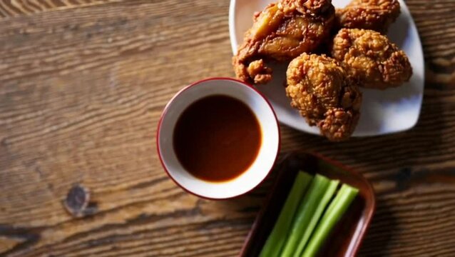 Vertical shot of delicious crispy fried chicken, ketchup, gravy and celery sticks on a wooden table
