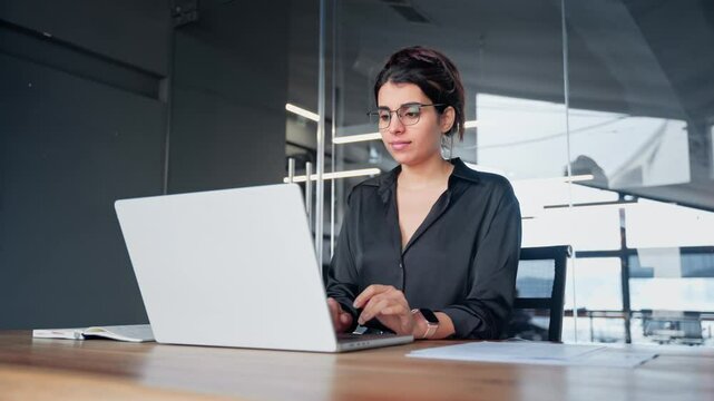 Focused busy female latin or arabian young business woman hr working on laptop computer reading finance document report, contract in office. Saleswoman manager businesswoman doing paperwork using pc