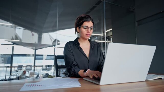 Busy latin or arabian young business woman hr working on laptop computer reading finance document report, cv contract in office. Accountant saleswoman manager businesswoman doing paperwork using pc