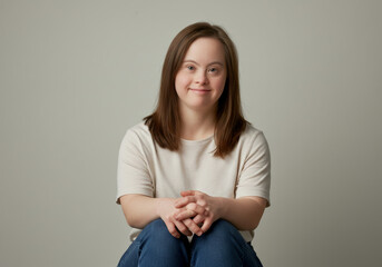 Young woman with down syndrome seated in relaxed pose against neutral background, engaging smile, warm expression, emphasizing positivity, diversity, and genuine character, soft lighting