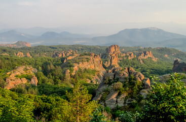 Obraz premium Belogradchik Rocks in Bulgaria with tall sandstone formations surrounded by green vegetation and distant hills, showing a natural geological landscape and a historic Balkan tourist destination