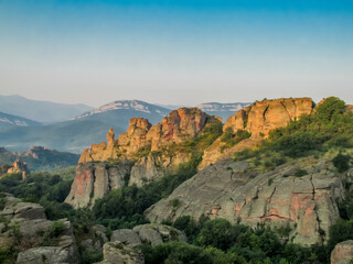 Fototapeta premium Belogradchik Rocks in Bulgaria with tall sandstone formations surrounded by green vegetation and distant hills, showing a natural geological landscape and a historic Balkan tourist destination