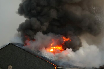 Building roof on fire. Strong red flame and black smoke raising high into the sky