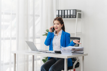 Portrait of beautiful businesswoman talking on the phone and working on laptop while sitting in...