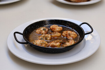 Gambas Pil Pil Spanish dish served in traditional cast iron pan ,white plate on table top down photo