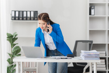 Portrait of beautiful businesswoman talking on the phone and working on laptop while sitting in...