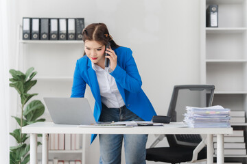 Portrait of beautiful businesswoman talking on the phone and working on laptop while sitting in...