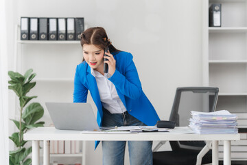 Portrait of beautiful businesswoman talking on the phone and working on laptop while sitting in...