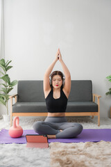 Online Yoga Class: A woman performs a side bend yoga pose on a purple mat at home, following...