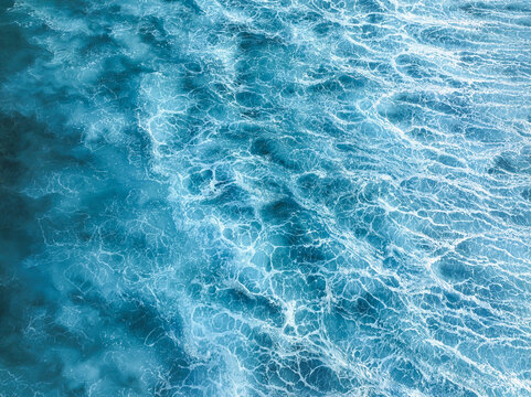Aerial view of turquoise waters dance with frothy white crests, forming intricate patterns across the vast expanse of the ocean at the surf spot Cokes, Thulusdhoo, Kaafu Atoll, Maldives.