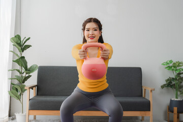 Strong core and healthy body: A cheerful woman is working out with a kettlebell in living room. The...