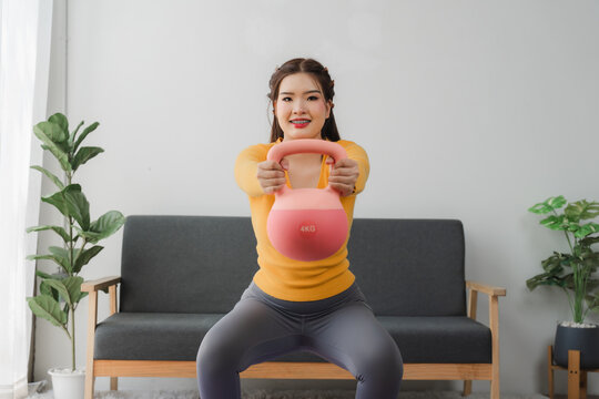 Strong core and healthy body: A cheerful woman is working out with a kettlebell in living room. The room is minimalist design and focus on her healthy lifestyle.