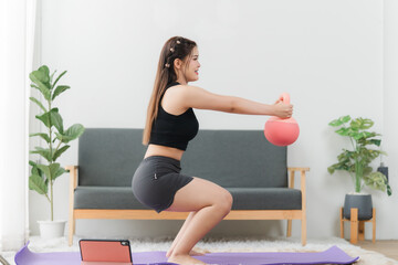 Home Workout: A young, athletic woman performs a squat exercise with a kettlebell. This dynamic...