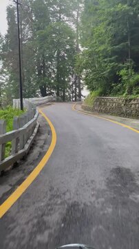 Bike ride on the scenic Government House track in Murree, Pakistan. Front view with speedometer, yellow-lined road, white wooden fence, and tall trees along the peaceful path in pleasant weather.

