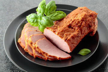 Smoked ham with basil on a black plate.