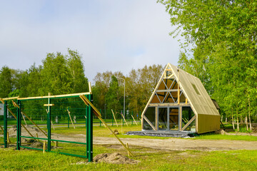 New A-Frame Glamping Cabin Under Construction in a Forested Campground with Green Fence Nearby