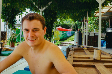 A young man enjoys his time outside, surrounded by greenery and sunlight, smiling cheerfully at a tropical resort. Taken on 35mm film.