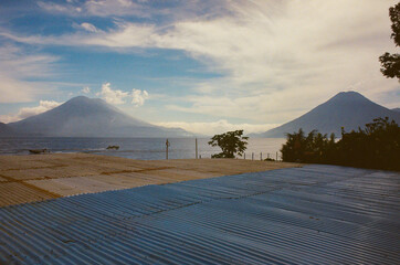 Lake Atitlán with two impressive volcanic peaks in the background. Surrounded by rooftops, nature and boats driving by. Capturing the serene beauty and atmosphere of a picturesque tropical landscape.