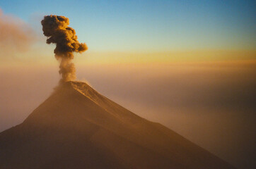 Fuego volcano spews dense smoke into the air, set against a serene dusk landscape with vibrant hues...