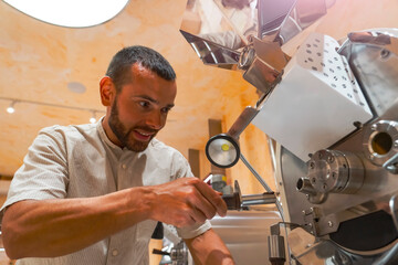 A skilled worker adjusts a coffee roasting machine to prepare arabica and robusta beans, showcasing the art of coffee preparation in a busy workshop filled with rich aromas