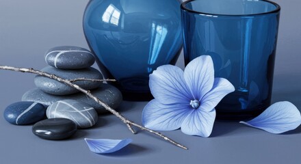 Serene still life featuring smooth stones, blue glassware and a delicate blue flower blossom.