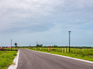 Perspective of a new suburban street, part of a planned community in progress, with grassy lots marked for house construction, in a residential development on a cloudy day in southwest Florida