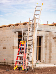 Aluminum extension and A-frame ladders leaning together against one corner of the concrete shell of a single-family house under construction on a cloudy morning in southwest Florida