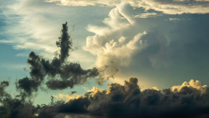Cloudscape with one anomalous cloud in prominent silhouette, as if upended by an updraft, during golden hour on a humid evening early in summer, southwest Florida. Motifs of local unpredictability.