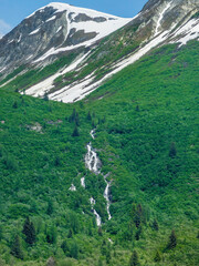 Segmented waterfall in a green valley below ice and snow high up a mountainside in Glacier Bay National Park, mid June in southeastern Alaska. Motifs of wild America.