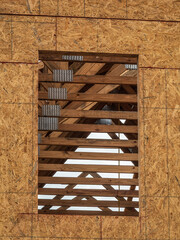 Window opening in exterior wall of a single-family house under construction, with partial interior view of wooden beams and roof trusses, on a cloudy morning in southwest Florida. (Low-angle view.)
