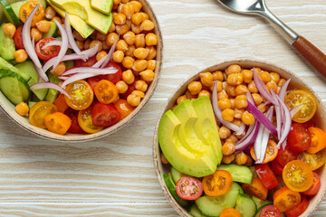 Two bowls of healthy chickpea salad with ripe avocado, juicy cherry tomatoes, crisp cucumber, and red onion slices. Perfect for a nutritious and healthy meal