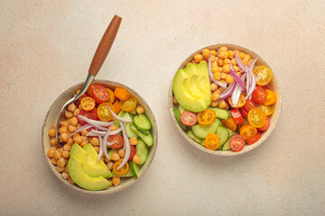 Two bowls of healthy chickpea salad with ripe avocado, juicy cherry tomatoes, crisp cucumber, and red onion slices. Perfect for a nutritious and healthy meal, light beige background