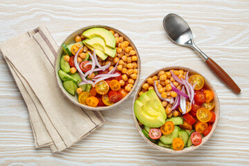Two bowls of healthy chickpea salad with ripe avocado, juicy cherry tomatoes, crisp cucumber, and red onion slices. Perfect for a nutritious and healthy meal