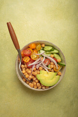 Healthy chickpea salad with ripe avocado, juicy cherry tomatoes, crisp cucumber, and red onion slices. Perfect for a nutritious and healthy meal on light green background