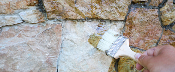 A brush applies a clear coating to an exterior natural stone wall. The wall, composed of...
