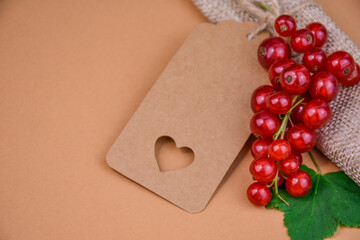 Summer arrangement with fresh redcurrants, burlap roll, green leaf and craft paper gift tag with...