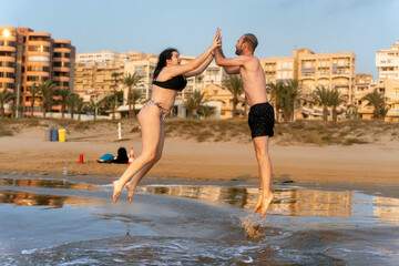Happy couple jumping and touching hands on the beach at sunrise