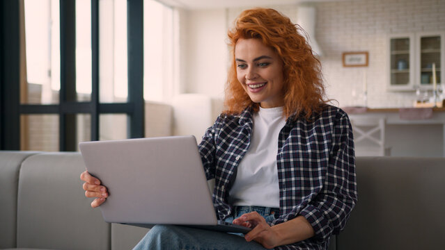 Smiling laughing fun communicate video call conference virtual chat laptop Caucasian woman on couch happy girl female chatting computer internet talking online at home laugh joke with friend remote