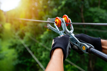 Close up of gloved hands holding a zipline pulley system with a forest background