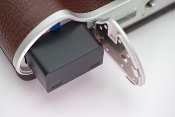 Detailed view of a camera battery compartment opened to reveal a black battery in a vintage styled...
