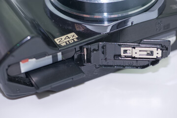 Camera showcasing a 24x wide zoom lens with an open compartment for battery and memory card access