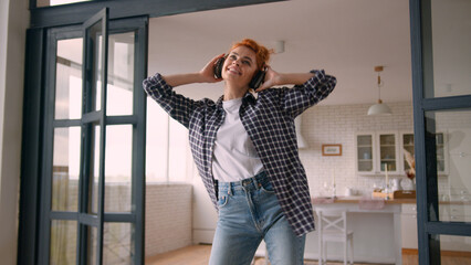 Happy smiling moving having fun fooling relaxing domestic dancing Caucasian woman girl female at home couch enjoy dance listening music in wireless headphones listen song audio sound freedom excited