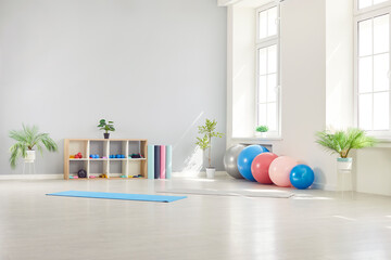 Interior of empty fitness gymnasium for yoga classes with sport equipment of fit balls and mats on the floor. Panoramic view of rehabilitation gym in medical clinic for physical treatment.