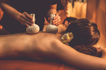 Hot herbal ball spa massage body treatment, masseur gently compresses herb bag on couple customer...