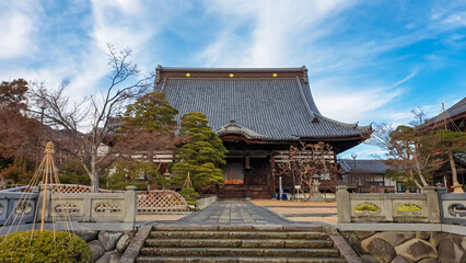 The magnificent main hall (Hondo) of the historic Zenko-ji Temple stands under a blue sky, viewed from the stone pathway leading to the entrance of this famous Buddhist landmark in Nagano.