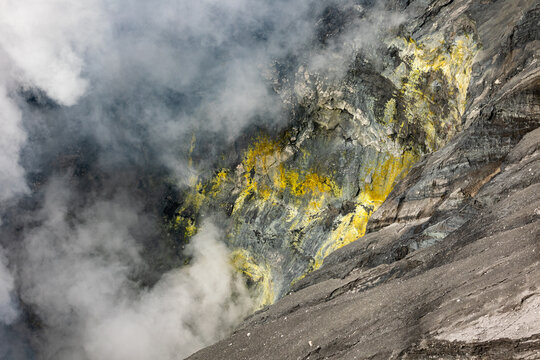 View of volcanic crater spewing white smoke and sulfurous yellow deposits clinging to the dark, rocky walls, Mount Bromo, East Java, Indonesia.