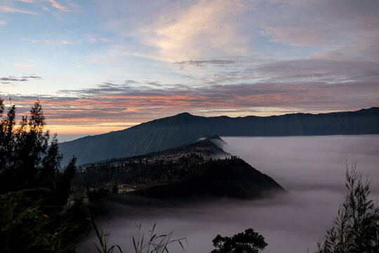 View of a volcanic landscape shrouded in a sea of mist under a vibrant, pastel-colored sky at dawn, Mount Bromo Volcano, East Java, Indonesia.