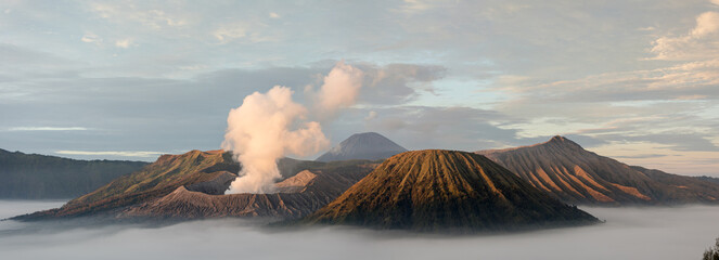 View of majestic volcanoes pierce through a sea of ethereal mist, with wisps of smoke rising from the crater, Mount Bromo Volcano, East Java, Indonesia.